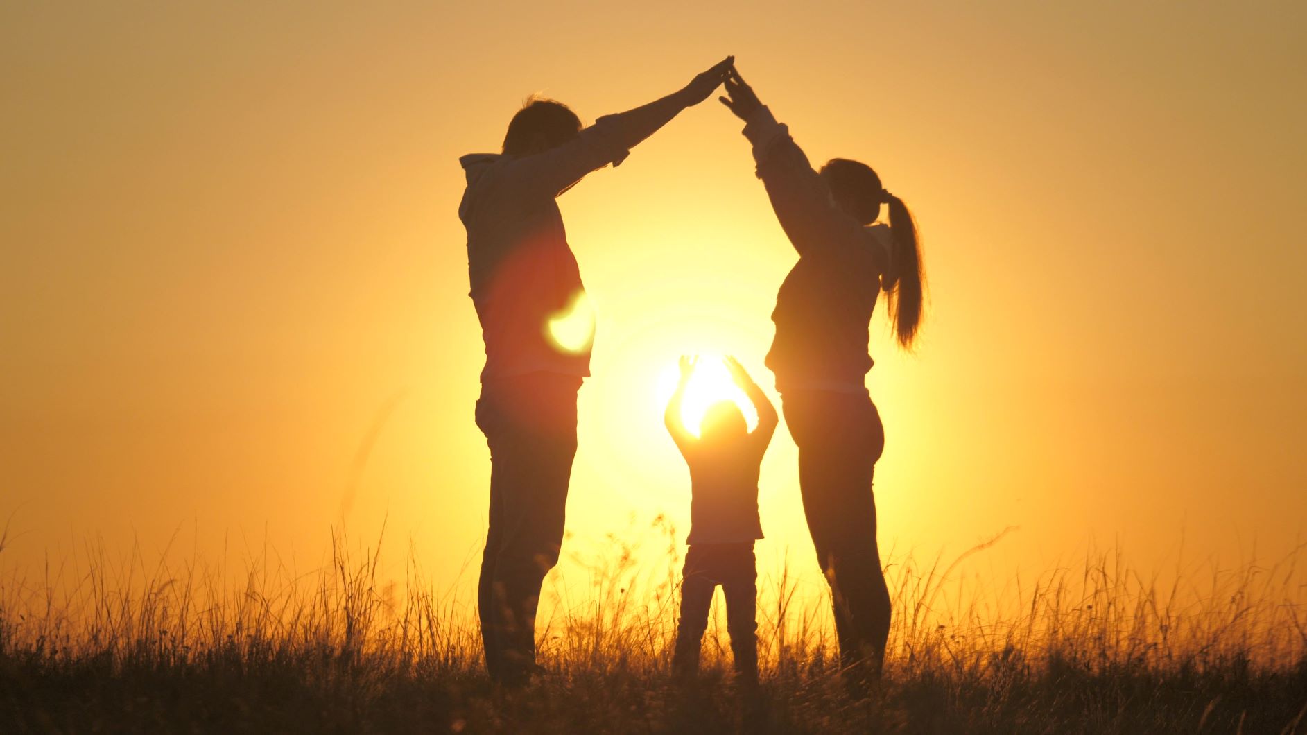 6439b07b21b4494d0c2ca67f_Transfer of Wealthb - shutterstock_1820747234 - The Gatsby Showcase Foundation Silhouetted family of three at sunset, two adults and a child, holding hands overhead as the sun sets behind them.
