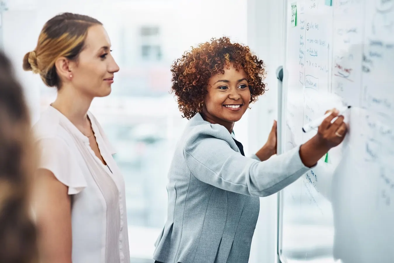 0x0 1 - The Gatsby Showcase Foundation Smiling Black woman writes on a whiteboard during a collaborative team planning session in a bright office.
