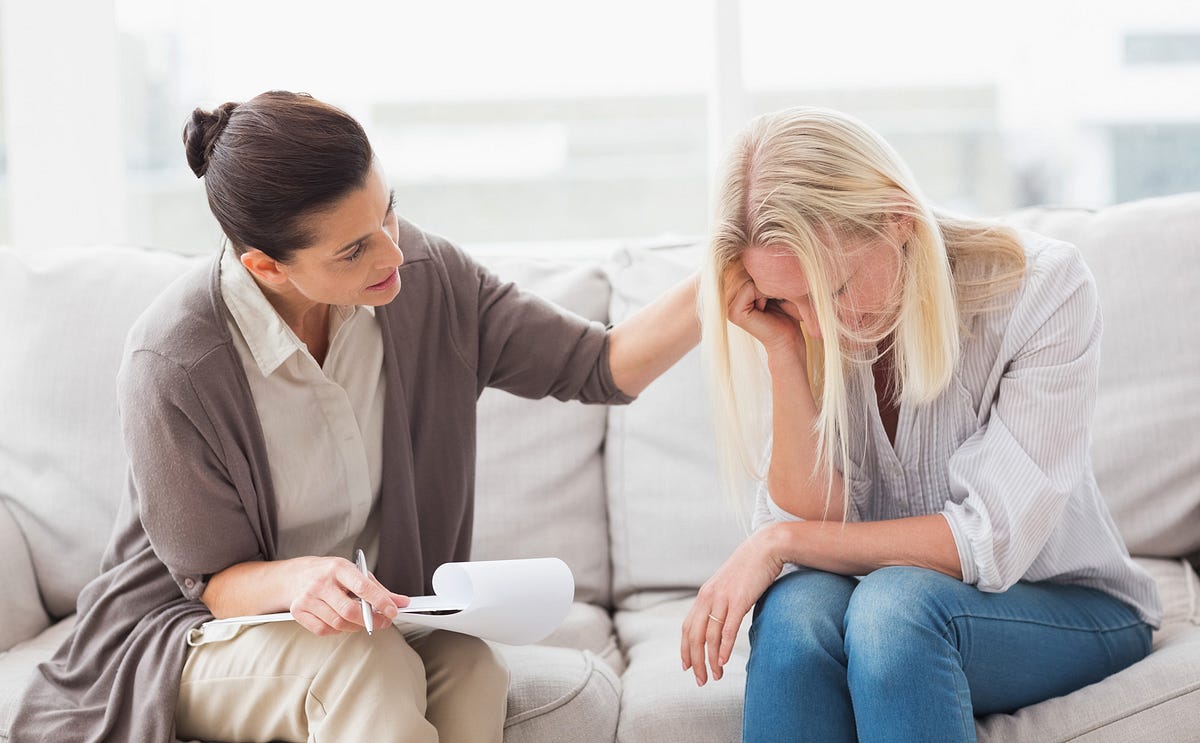 1_8RU80tmjaY8yLz2howNn-g - The Gatsby Showcase Foundation Counselor sits with a distressed client on a sofa, offering support while taking notes.
